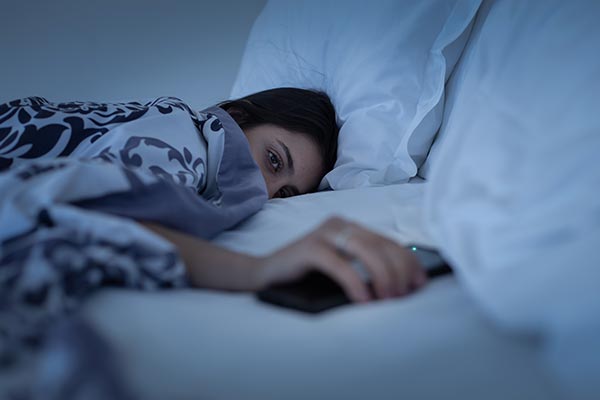Young girl reaching for her phone in bed struggling with sleep care